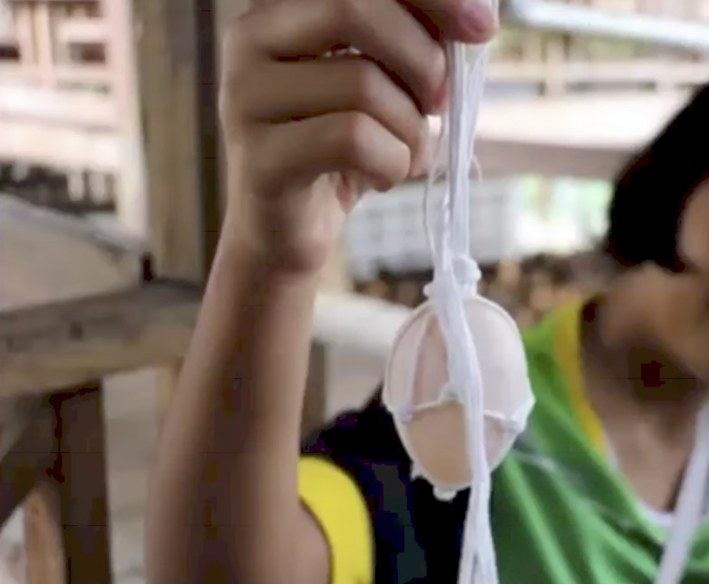 A student holding up a raw egg protected inside a hand-knotted string net